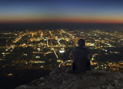 A man standing on a hill over a town at dusk. He's pondering his kingdom impact.