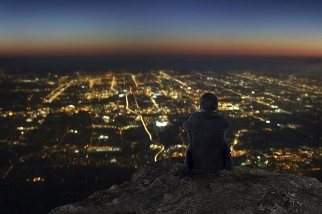 A man standing on a hill over a town at dusk. He's pondering his kingdom impact.