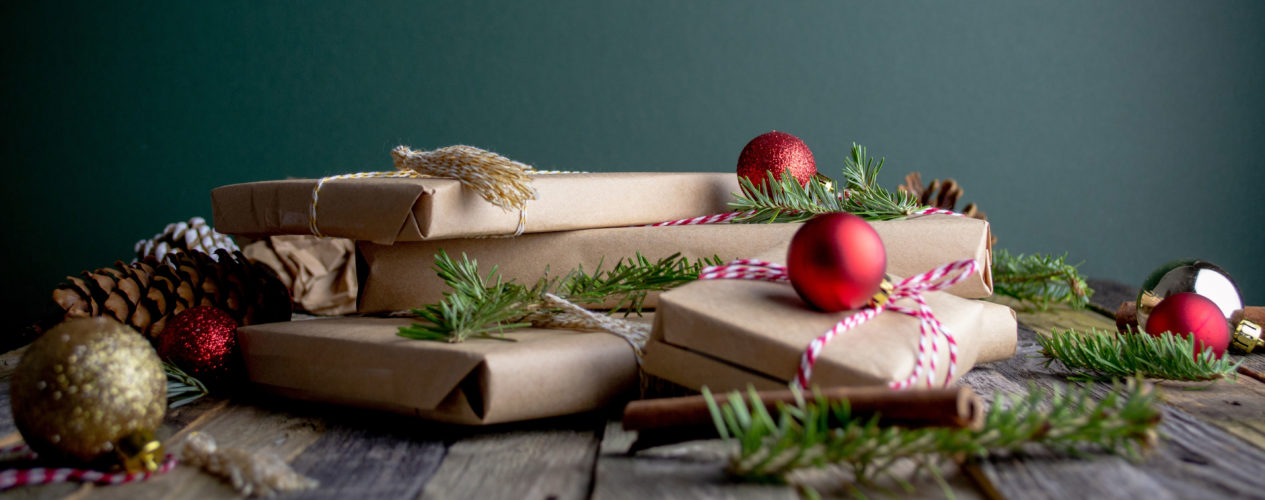Gifts wrapped in brown paper with red ornaments and pine branches on top of the presents.